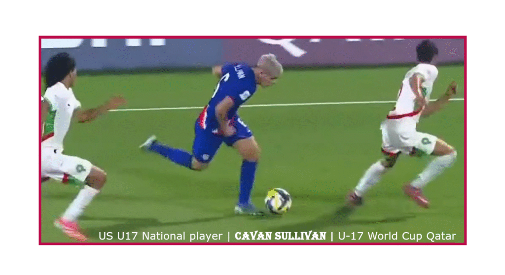 Cavan Sullivan of the United States sprints with the ball during a U-17 World Cup Qatar match, pursued by El Mahdi Saidi and Hamza Bouhaddi of Morocco. Sullivan wears a blue USSF kit, while the Moroccan players wear white. The scene captures high-speed midfield action on a green pitch with advertising boards in the background.