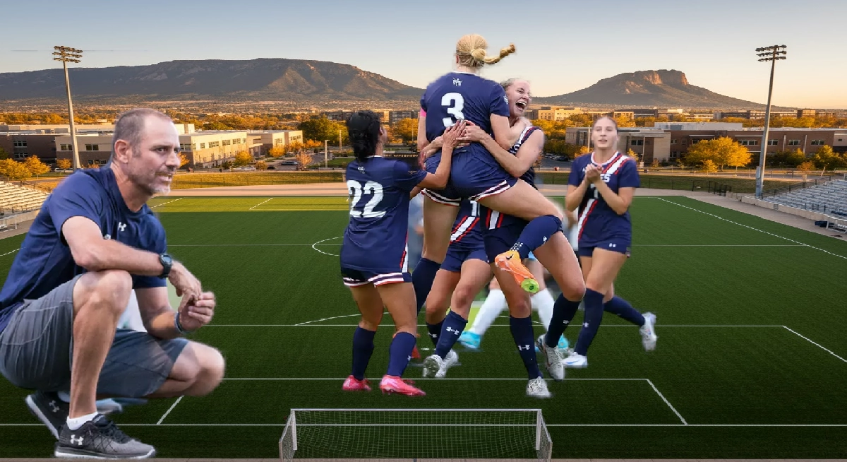 Colorado School of Mines women’s soccer players celebrate on the field with Head Coach Kevin Fickes observing from the sideline. One player is lifted into the air by a teammate while others clap and smile. The team wears navy uniforms with white and red accents. The scene includes stadium seating, buildings, and a mountain backdrop under a clear sky.
