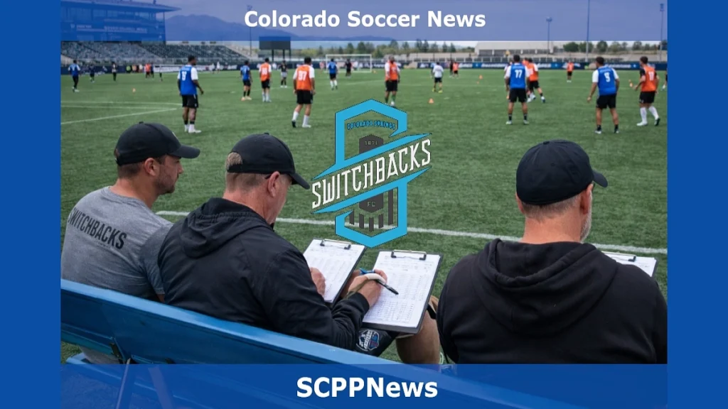Colorado Springs Switchbacks FC staff seated on a bench evaluating players during a soccer tryout on artificial turf, with athletes in orange and blue pinnies training in the background and the club logo centered in the image.