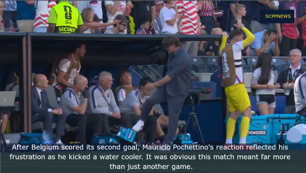 Mauricio Pochettino kicks a water cooler in frustration on the USMNT bench after Belgium’s second goal, with staff and substitutes seated nearby in a crowded stadium.