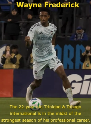 Wayne Frederick, wearing a light gray soccer uniform and captain’s armband, controls the ball during a match with spectators and advertising boards in the background. Text on the image highlights that the 22‑year‑old Trinidad and Tobago international is having the strongest season of his professional career.